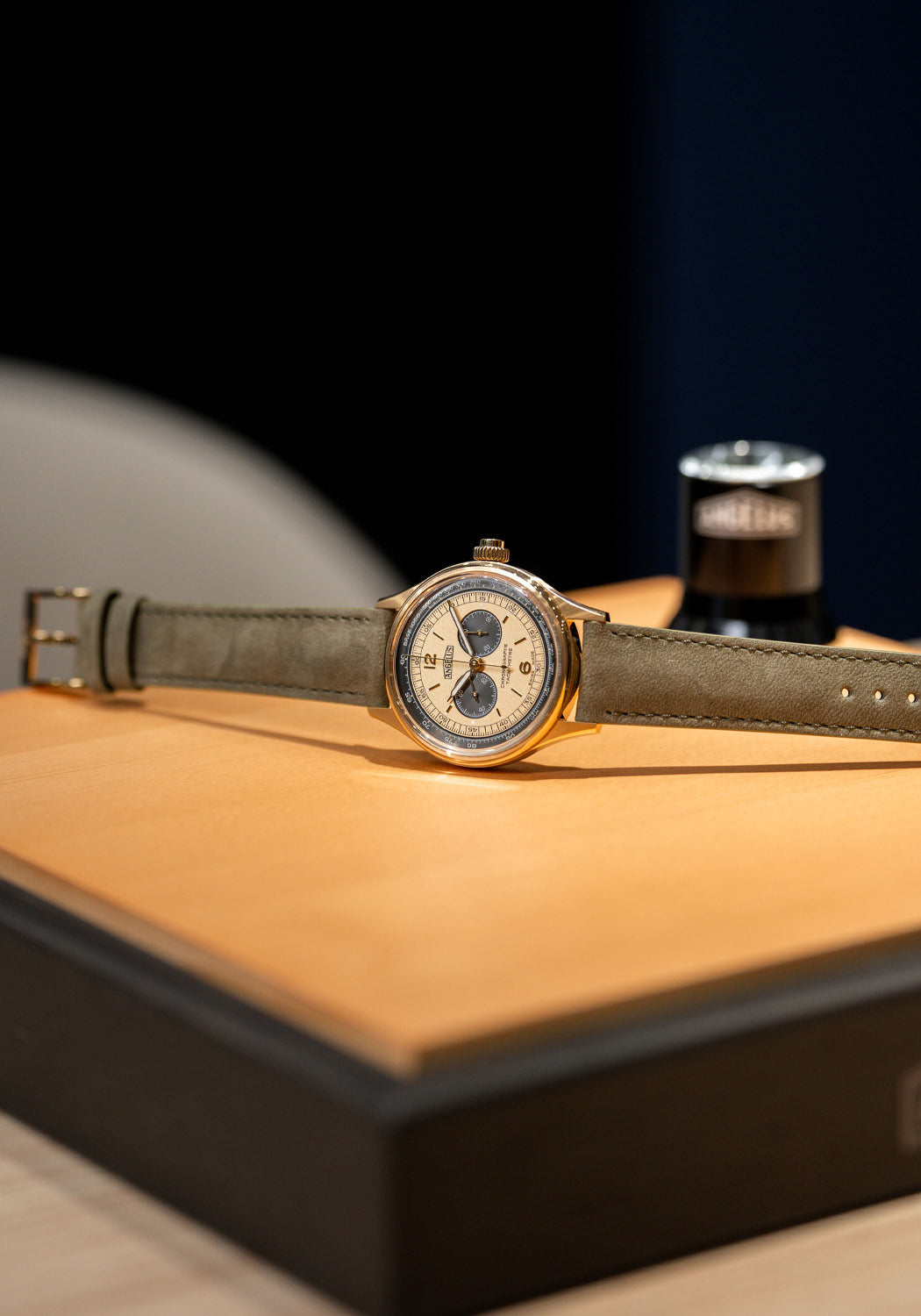 A stylized shot of the Angelus Chronographe Tachymètre Yellow Gold on its side on a wood box