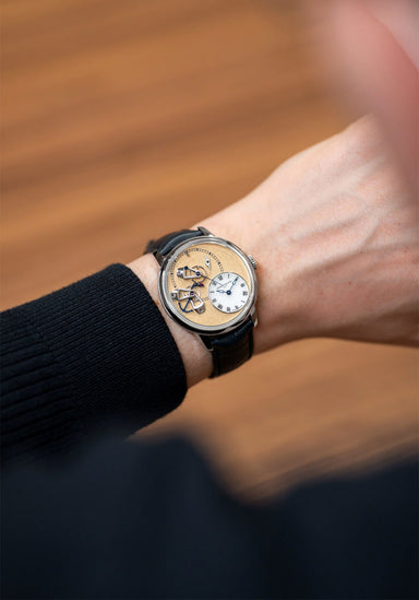 The Arnold & Son DSTB Stop-Seconds Platinum Kingsand on a man's wrist with a blurred wood background