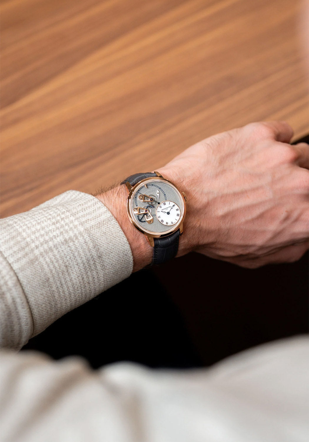 The Arnold & Son DSTB Stop-Seconds Red Gold Cliff Grey on a man's wrist in front of a wood floor