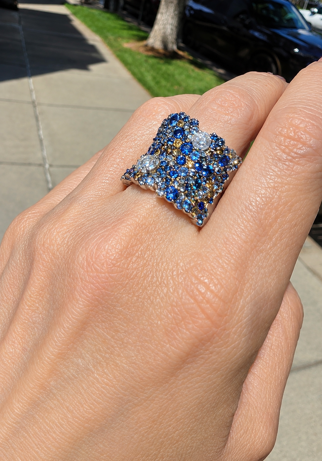 Hand wearing multi sized blue and white stone wide saddle ring at Osterjewelers.com