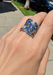 Hand wearing multi sized blue and white stone wide saddle ring at Osterjewelers.com