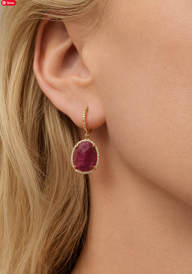 Blonde Woman wearing a slightly oval ruby earring surrounded by diamonds in 14 rose gold. Osterjewelers.com
