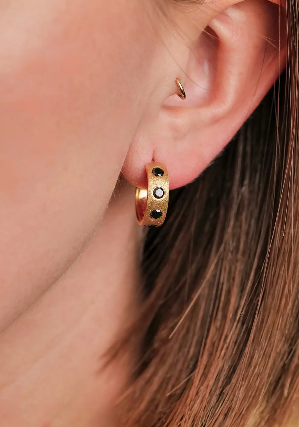 The Sethi Couture Dunes Black Diamond Huggie has a brushed gold finish. Shown on a model