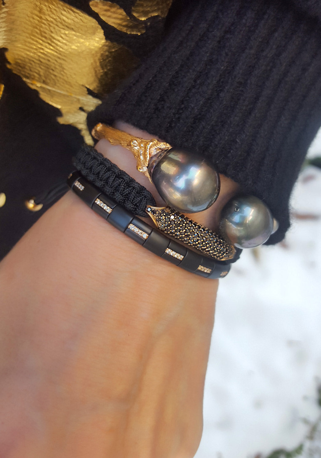 Woman wearing three bracelets. Pearl cuff, braided black diamond cord bracelet and stretch diamond bracelet at Oster Jewelers