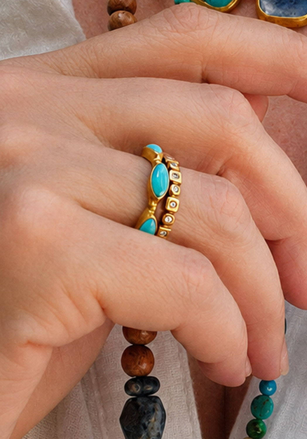A close-up of a hand wearing a gold ring set with oval turquoise stones. Oster Jewelers