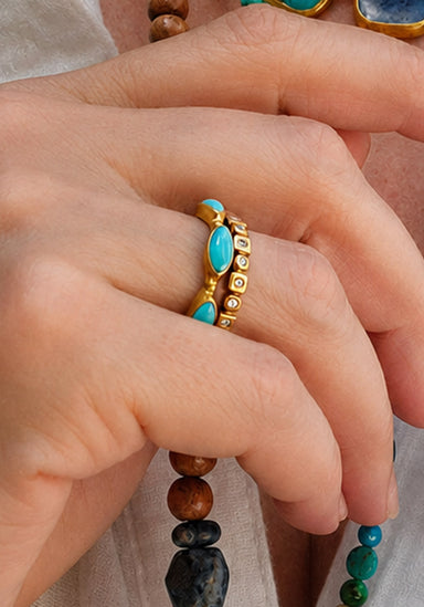 A close-up of a hand wearing a gold ring set with oval turquoise stones. Oster Jewelers
