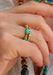 A close-up of a hand wearing a gold ring set with oval turquoise stones. Oster Jewelers