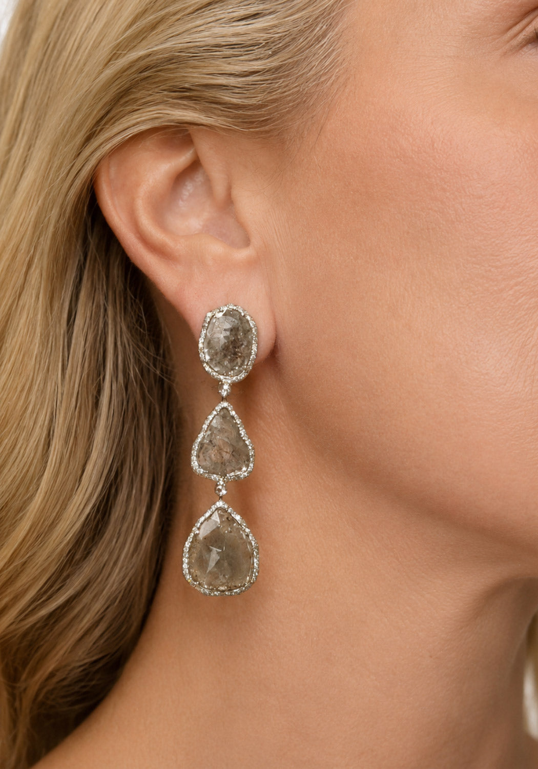 Blonde woman wearing oval, oblong and triaangular shaped grey diamond dangle earring.