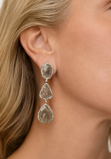 Blonde woman wearing oval, oblong and triaangular shaped grey diamond dangle earring.