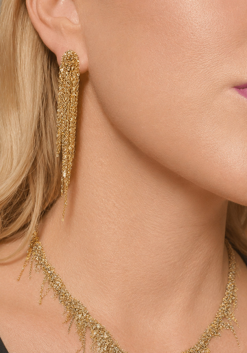 Close-up of a model wearing gold fringe necklace and long dangling gold earrings with a textured, glittery fringe design.