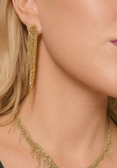 Close-up of a model wearing gold fringe necklace and long dangling gold earrings with a textured, glittery fringe design.