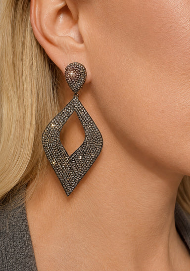 A close-up of a model's ear wearing a large, geometric cut-out drop earring encrusted with raw diamonds.