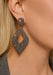 A close-up of a model's ear wearing a large, geometric cut-out drop earring encrusted with raw diamonds.
