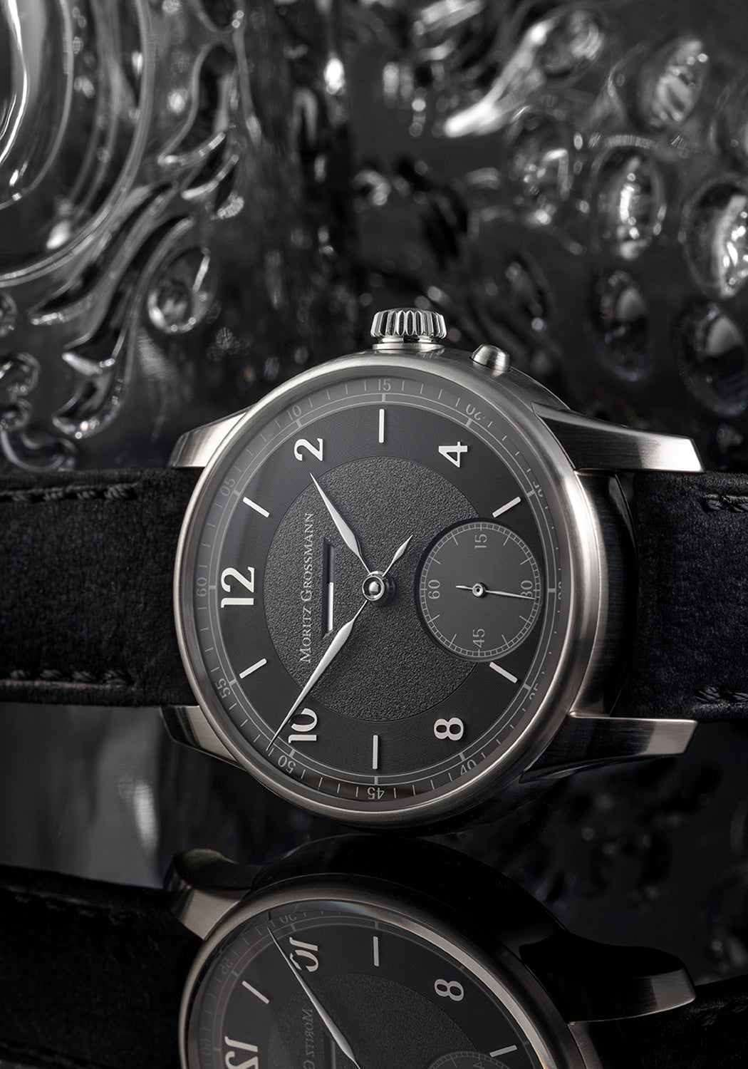 The Moritz Grossmann Benu Power Reserve Black Stainless Steel on a grey textured dial