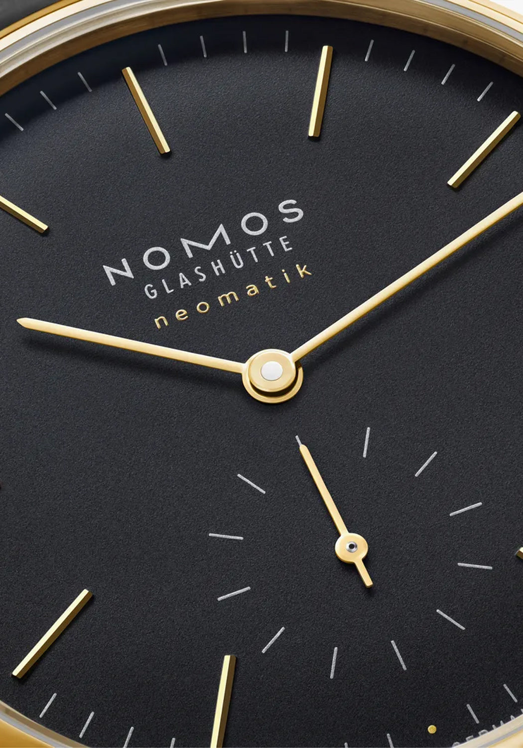 Closeup of the minimalist NOMOS Orion Gold Neomatik New Black dial showing the gold indexes & hands
