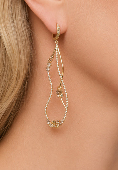Woman wearing multi colored fancy diamond curved open dangle earrings.