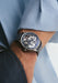 The Renaud Tixier Monday Skeleton Blue on a man's wrist wearing a blue shirt and denim jeans