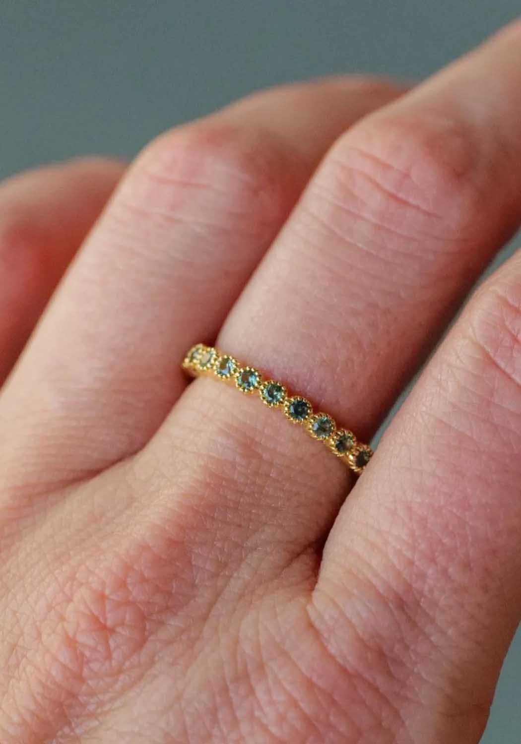 The Sethi Couture Bezel Mini Green Sapphire Eternity Band on a model's hand highlights the green hue