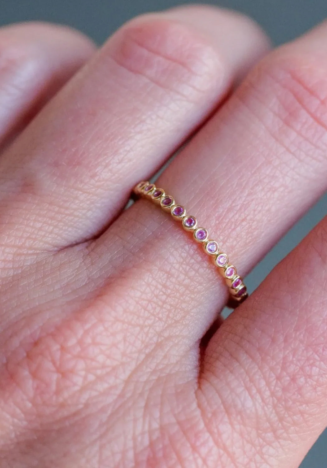 Closeup of the Sethi Couture Bezel 18KYG Mini Pink Sapphire Eternity Band on a model's hand
