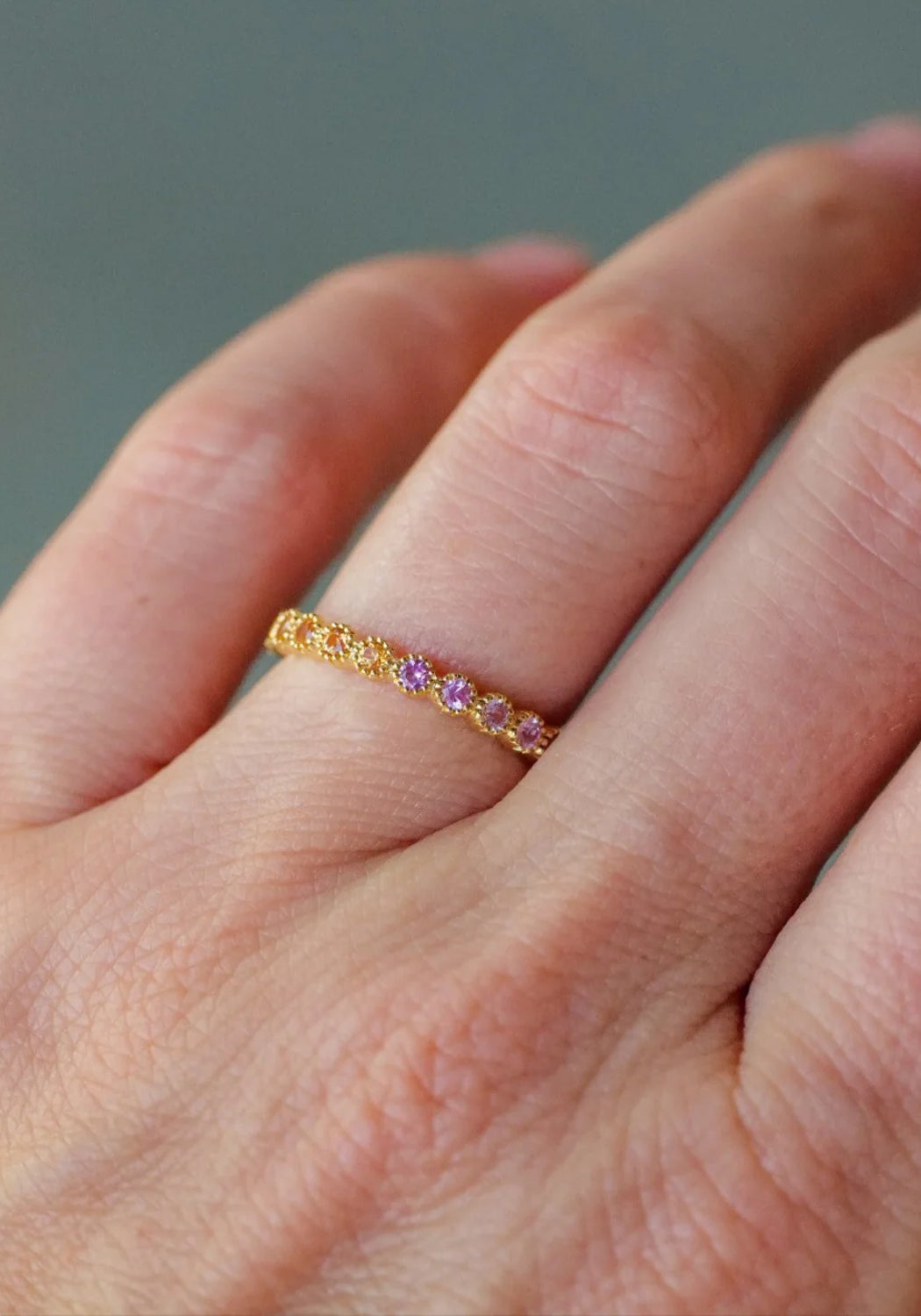 The colorful Sethi Couture Bezel 18KYG Rainbow Sapphire Eternity Band worn solo on a model's hand.