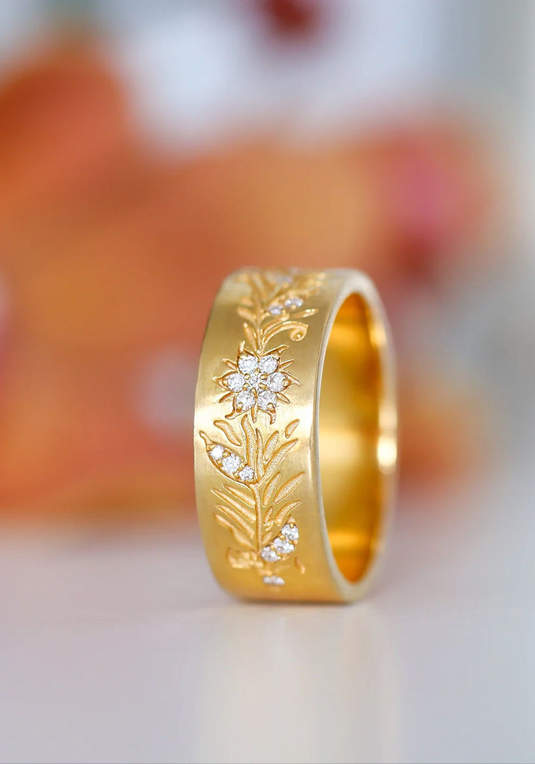 Sethi Couture Fleur 18KYG Wide Floral Diamond Band shown on its side on a blurred floral background