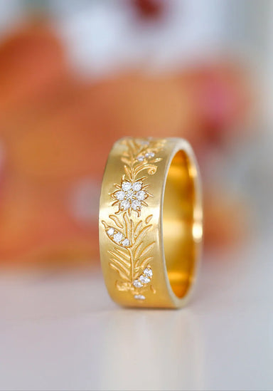 Sethi Couture Fleur 18KYG Wide Floral Diamond Band shown on its side on a blurred floral background