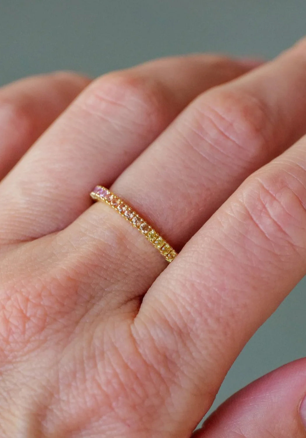 The colorful Sethi Couture Prong Rainbow Sapphire Eternity Band on a model's hand