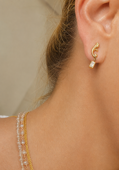 woman wearing a baguette diamond dangle earring with gold scroll detail.